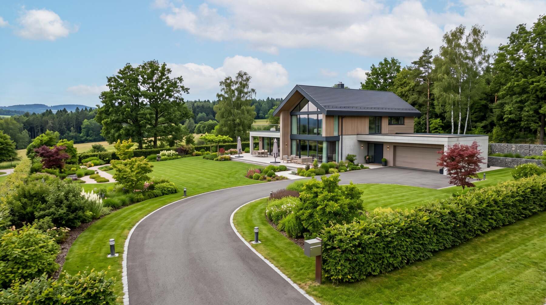 Modernes Einfamilienhaus mit großer Auffahrt, gepflegtem Garten und Terrasse in grüner Landschaft.